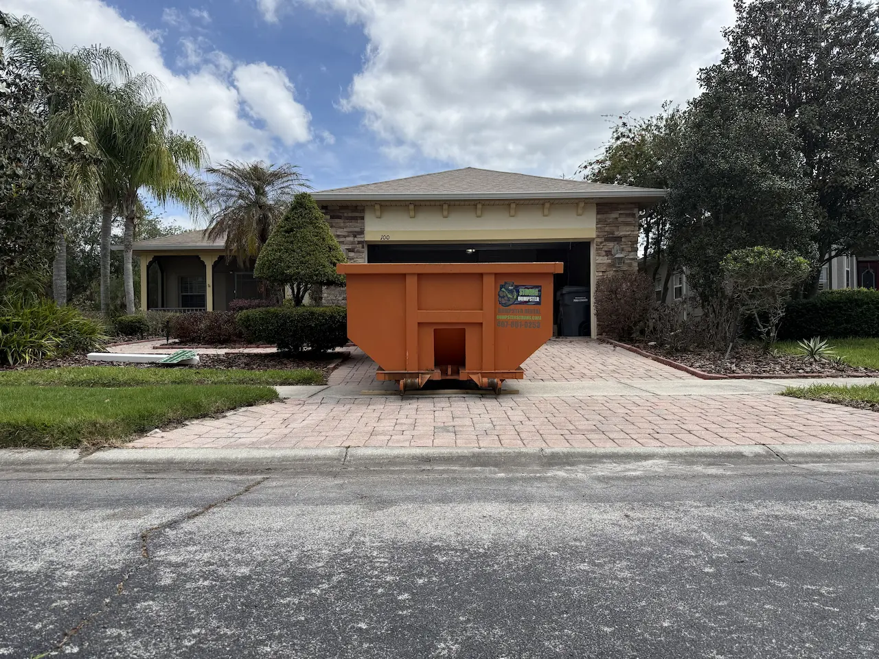 Orange Dumpster Strong roll-off dumpster on a residential driveway in Orlando, FL